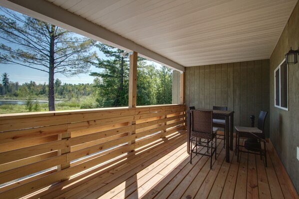A wooden deck with a table and chairs, overlooking a forested area.
