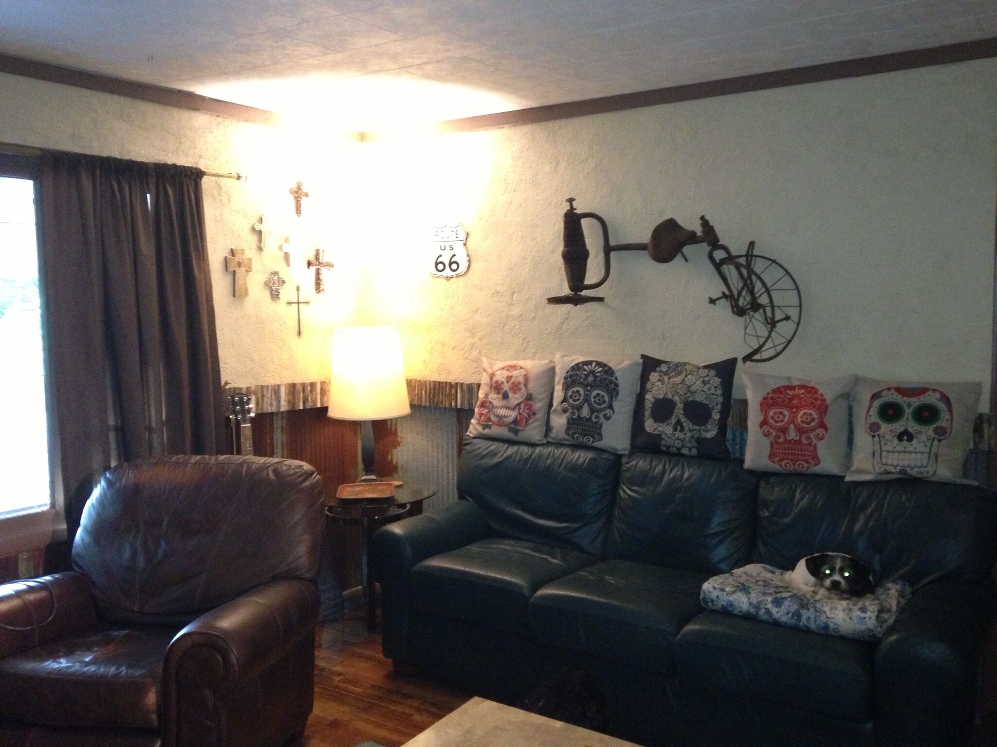 Een woonkamer met een leren bank, een houten salontafel en een lamp. Op de muur hangen decoraties, waaronder kruisen en een fiets.