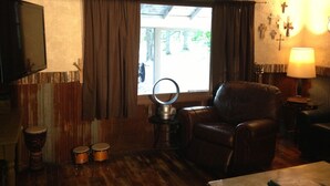 Ein Zimmer mit Ledersessel, Schlagzeug, Spiegel und einem Fenster mit Vorhängen.