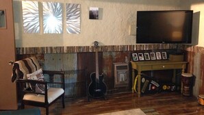 Ein Wohnzimmer mit Holzboden, einem an der Wand befestigten Fernseher, einer Gitarre und einem Schlagzeug.