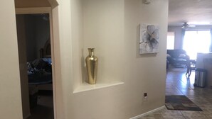 Un pasillo con un jarrón dorado en un estante, un cuadro en la pared y un suelo de baldosas.