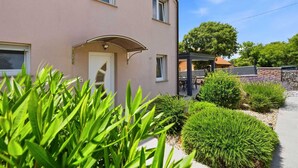A two-story building with a covered entrance, a patio area with outdoor seating, and a stone wall. - Holiday house Pink with Pool (Skrbčići)