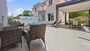 Un espace extérieur abrité doté d’une piscine, de meubles en osier et d’un bâtiment aux grandes fenêtres.