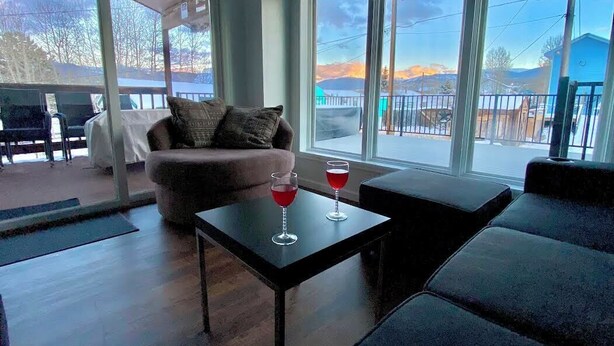 A modern living room with a sofa, a coffee table with two red drinks, and large windows offering a view of a snowy landscape.
