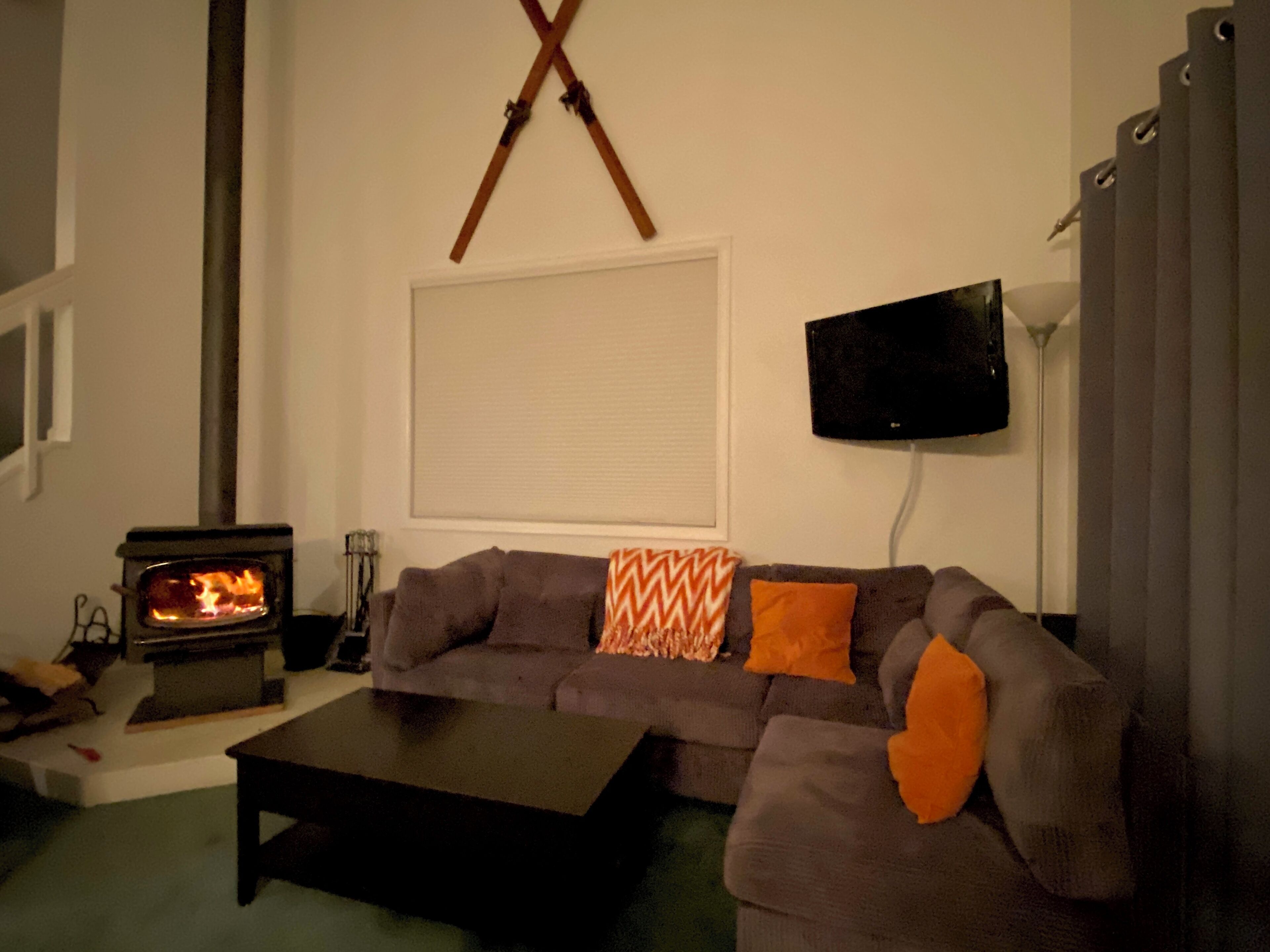 A living room with a sofa, a coffee table, a fireplace, a television mounted on the wall, and a window with blinds.