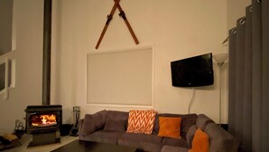 A living room with a sofa, a coffee table, a fireplace, a television mounted on the wall, and a window with blinds.