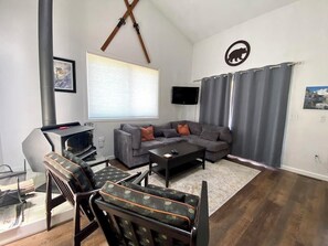 A living room with a sofa, coffee table, and chairs, a fireplace, a TV, and a mounted TV.