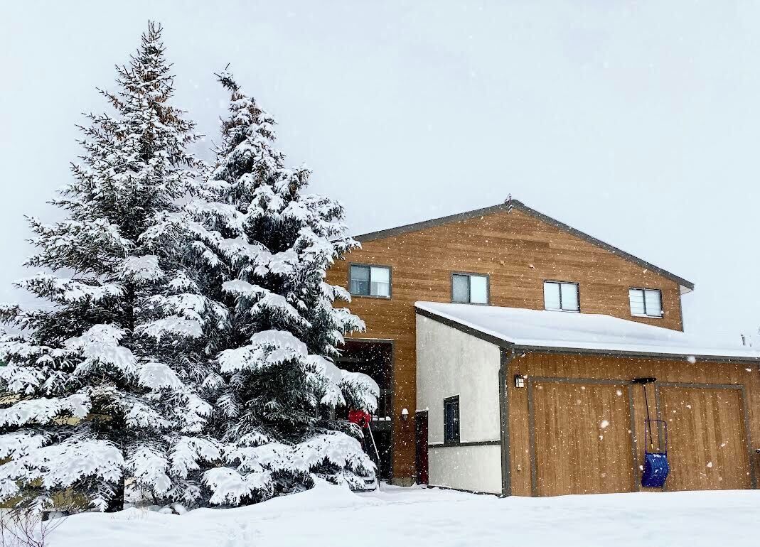 Un edificio de dos pisos con techo cubierto de nieve y un garaje adosado al lado derecho.