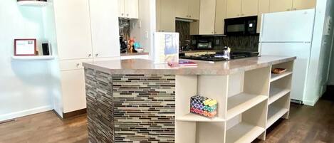 A modern kitchen with white cabinetry, a central island with a mosaic backsplash, and a built-in shelf unit.