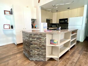 A modern kitchen with white cabinetry, a central island with a mosaic backsplash, and a built-in shelf unit.