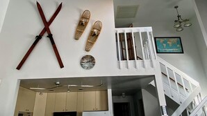 A modern interior with a large X-shaped wooden sculpture, woven wall hangings, a globe map, and a staircase.