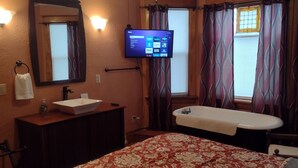Habitación de hotel con una cama grande, baño con lavamanos y espejo, televisor montado en la pared y cortinas estampadas.