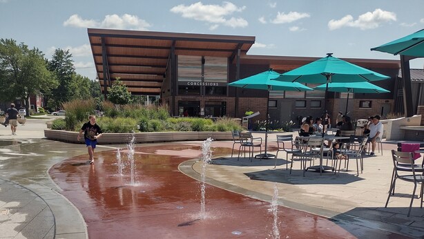 Una plaza pública con fuente de agua, asientos al aire libre y un edificio con el rótulo "CONCESSIONS" al fondo.