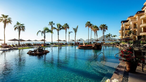 A clear blue pool with lounge chairs and palm trees, surrounded by a resort building. - Ocean view, swim-up bar, private balcony-Paradise! (Cabo San Lucas)