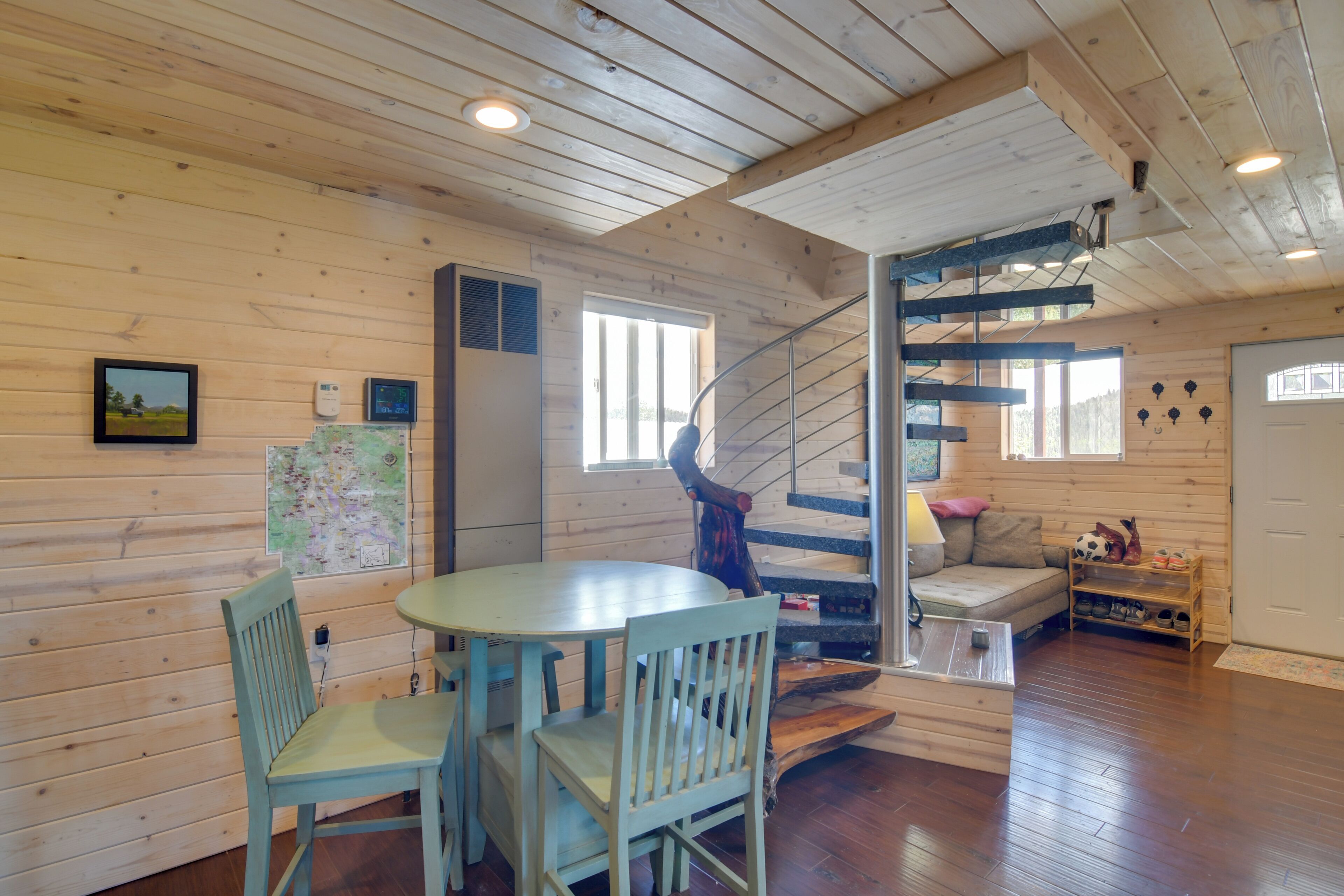 Un intérieur en bois avec un escalier en colimaçon, une table ronde entourée de chaises et un canapé.