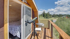 Eine Holzhütte mit einem Teleskop auf dem Balkon, einem Bett mit einem blattgemusterten Überwurf sowie einem kleinen Tisch und Stuhl.