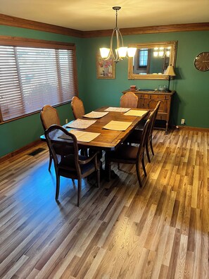 Un comedor con una mesa de madera, sillas, una araña, un espejo y un reloj en la pared.
