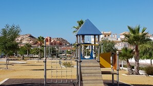Un parque infantil con estructura para escalar, tobogán y zona delimitada con red.
