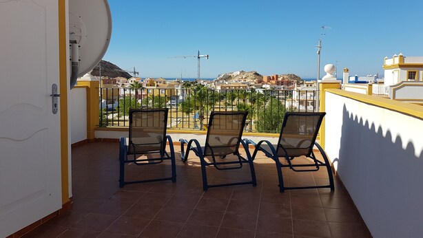 Un balcón con dos sillas, una antena parabólica y vistas a un pueblo costero.