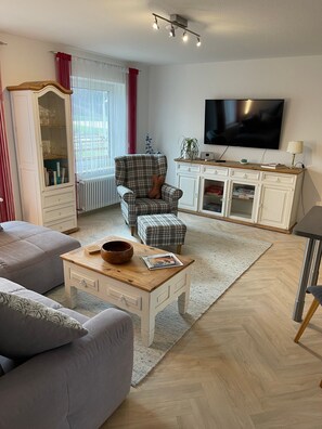 A living room with a sofa, armchair, coffee table, TV, and a cabinet.