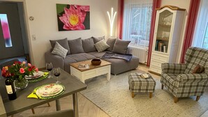 Una sala de estar con sofá, mesa de centro, mesa de comedor con un florero y estantería.