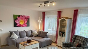 Una sala de estar con un sofá gris, un sillón escocés, una mesita de centro y una estantería.