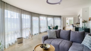 A modern living room with a grey sofa, a wooden coffee table, and sheer curtains.