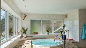 A modern bathroom with a large bathtub, a window with a view, and several potted plants.