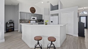 A modern kitchen with a central island, two bar stools, and a clock on the wall. - St Lucie Central Cozy Casa (Port St. Lucie)