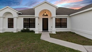 A two-story house with a central entrance, a covered porch, and a small front yard. - St Lucie Central Cozy Casa (Port St. Lucie)