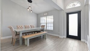 A dining area with a light-colored table and bench, upholstered chairs, and a ceiling light fixture. - St Lucie Central Cozy Casa (Port St. Lucie)