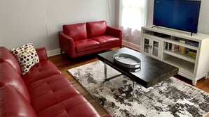 A living room with a red leather sofa, a coffee table, a flat-screen TV, and a bookshelf.