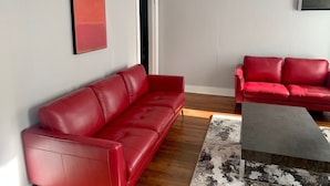 A modern living room with two red leather sofas, a black coffee table, a red abstract painting, and a ceiling fan.