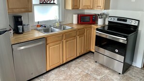 A kitchen with wooden cabinets, a stainless steel dishwasher, a red microwave, and a black oven.