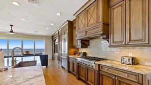 A kitchen with wooden cabinets, a granite countertop, and a view of the ocean.