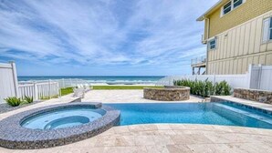 A swimming pool with a hot tub, a stone border, and a view of the ocean.