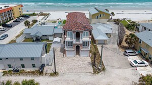 A coastal residential area with a prominent house featuring a tiled roof, a front porch, and a driveway.