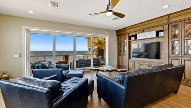 A spacious living room with a large TV, leather sofas, and a view of the ocean.