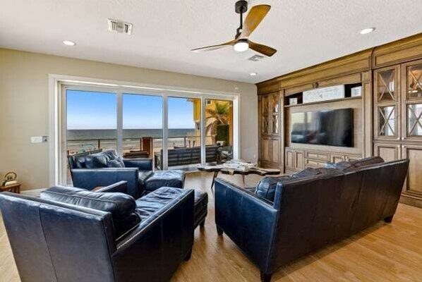 A spacious living room with a large TV, leather sofas, and a view of the ocean.