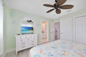 Un dormitorio con cama, cómoda, televisor y ventilador de techo.
