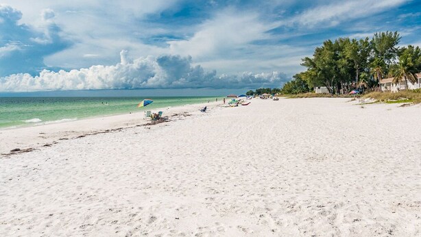 Ein weiter Sandstrand mit vereinzelten Sonnenschirmen und Liegestühlen, ein klarer Himmel und ein Blick auf den fernen Ozean.