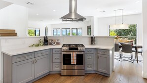 Una cocina moderna con armarios grises, una campana extractora de acero inoxidable y un amplio ventanal con vistas a un balcón.