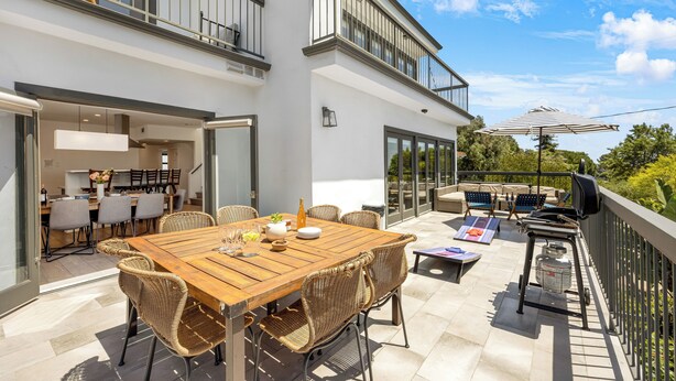 Un espacio moderno para comer al aire libre, con una mesa de madera y sillas de mimbre, una parrilla y un parasol.