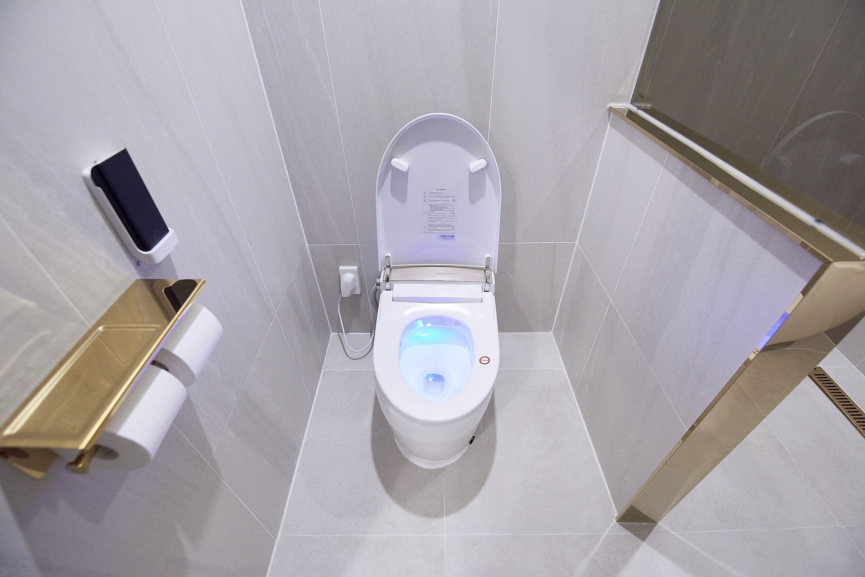 Des toilettes modernes dotées d’un écran numérique, d’un porte-rouleau de papier toilette et d’un distributeur de gel hydroalcoolique.
