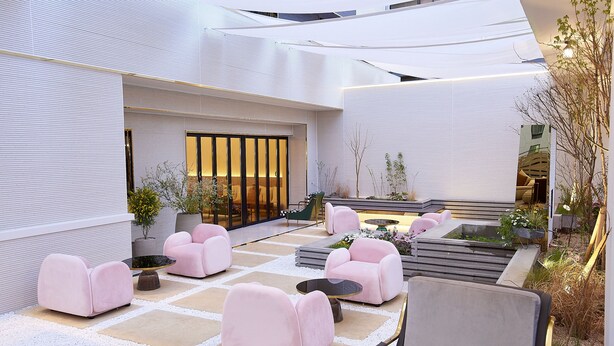 A modern outdoor seating area with cushioned chairs and tables, surrounded by a white exterior wall and a small water feature. - Den Basta Signature Hotel (Busan)