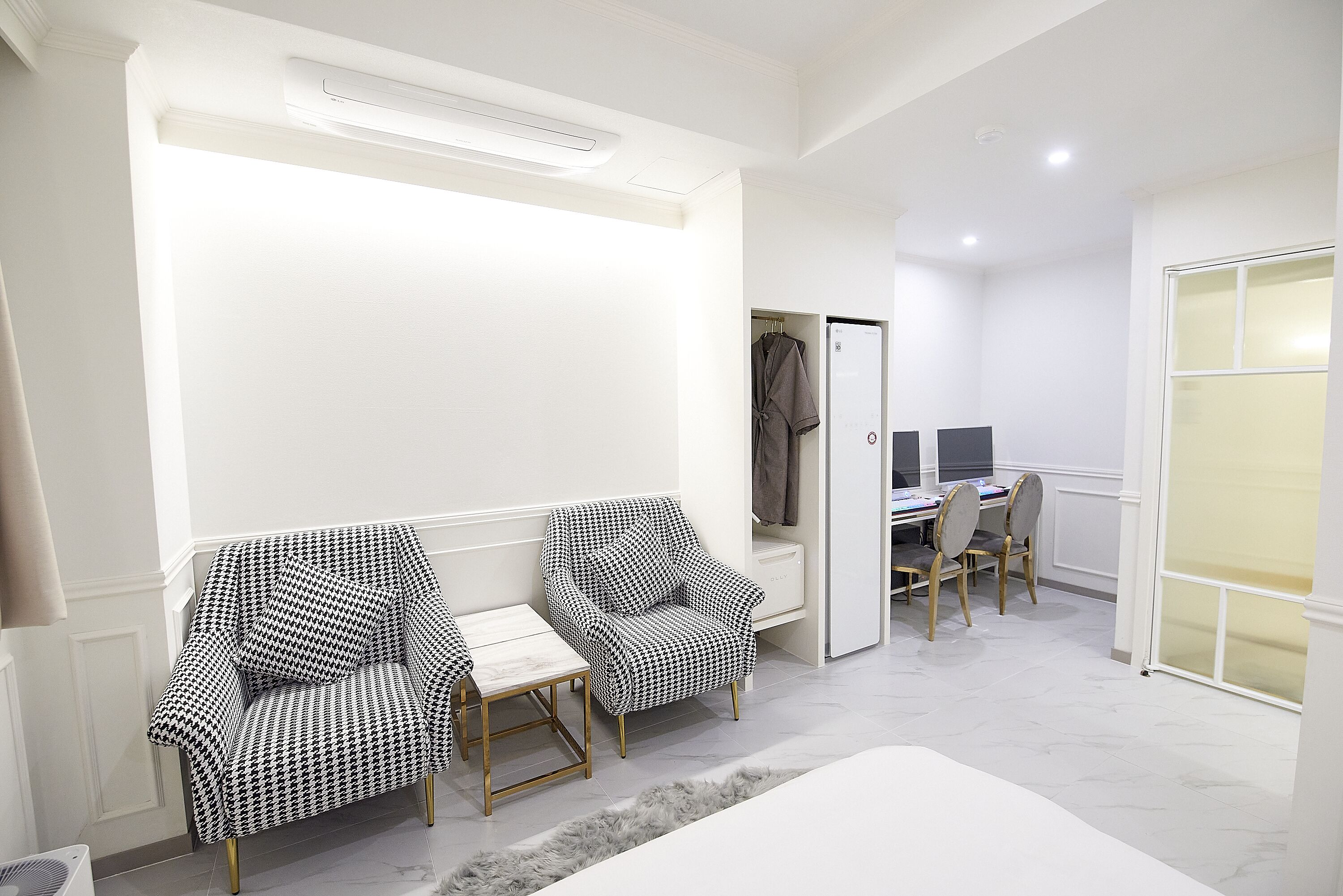 A room with two patterned armchairs, a small table, a desk with two chairs, and a wardrobe.