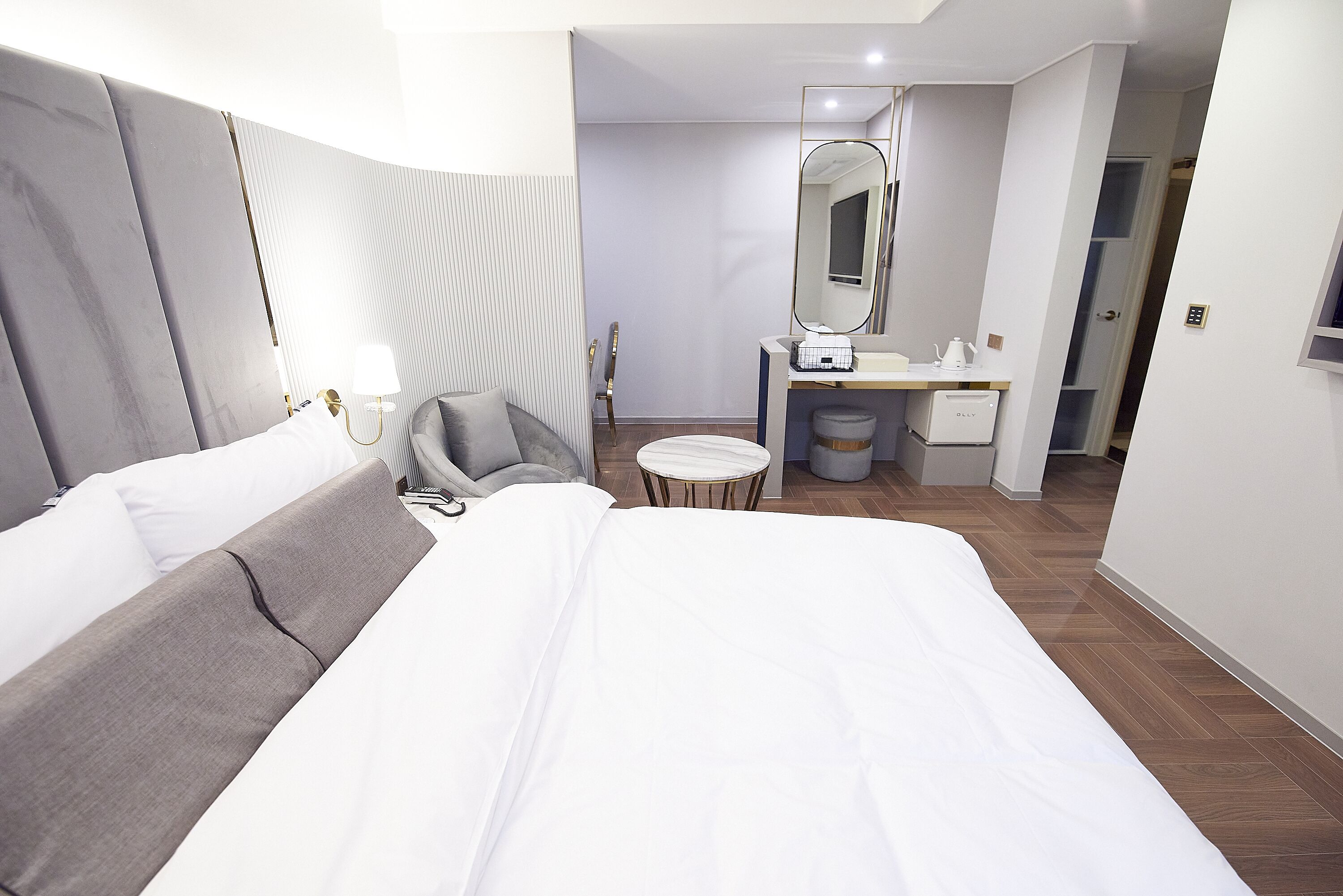 Une chambre d’hôtel moderne avec un grand lit, une table de chevet, une chaise, une petite table ronde, un miroir et une armoire.