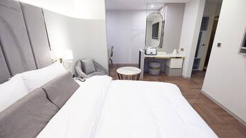 Une chambre d’hôtel moderne avec un grand lit, une table de chevet, une chaise, une petite table ronde, un miroir et une armoire.