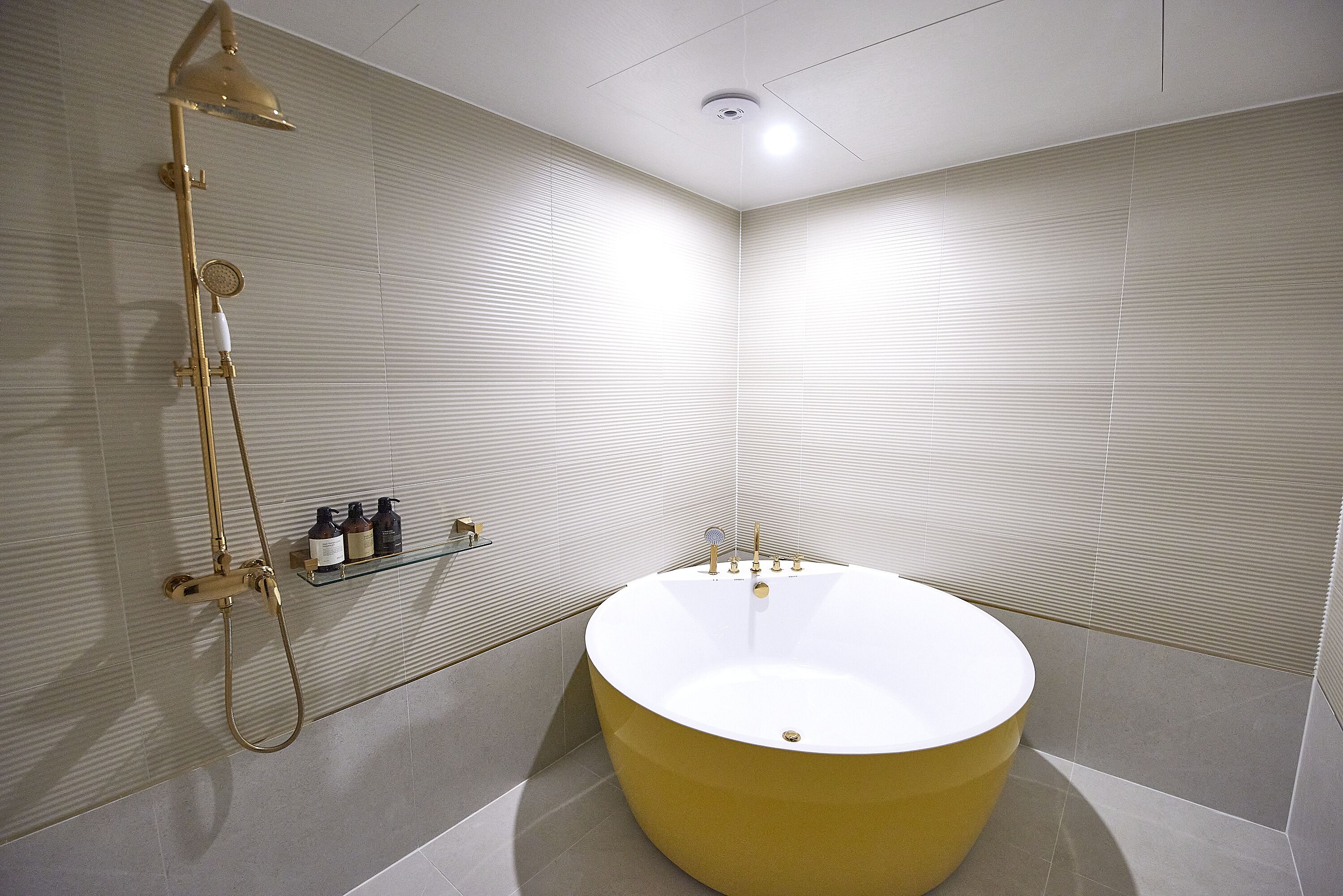 A modern bathroom with a large bathtub, a showerhead, and a shelf with toiletries.