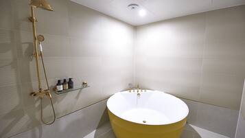 A modern bathroom with a large bathtub, a showerhead, and a shelf with toiletries.
